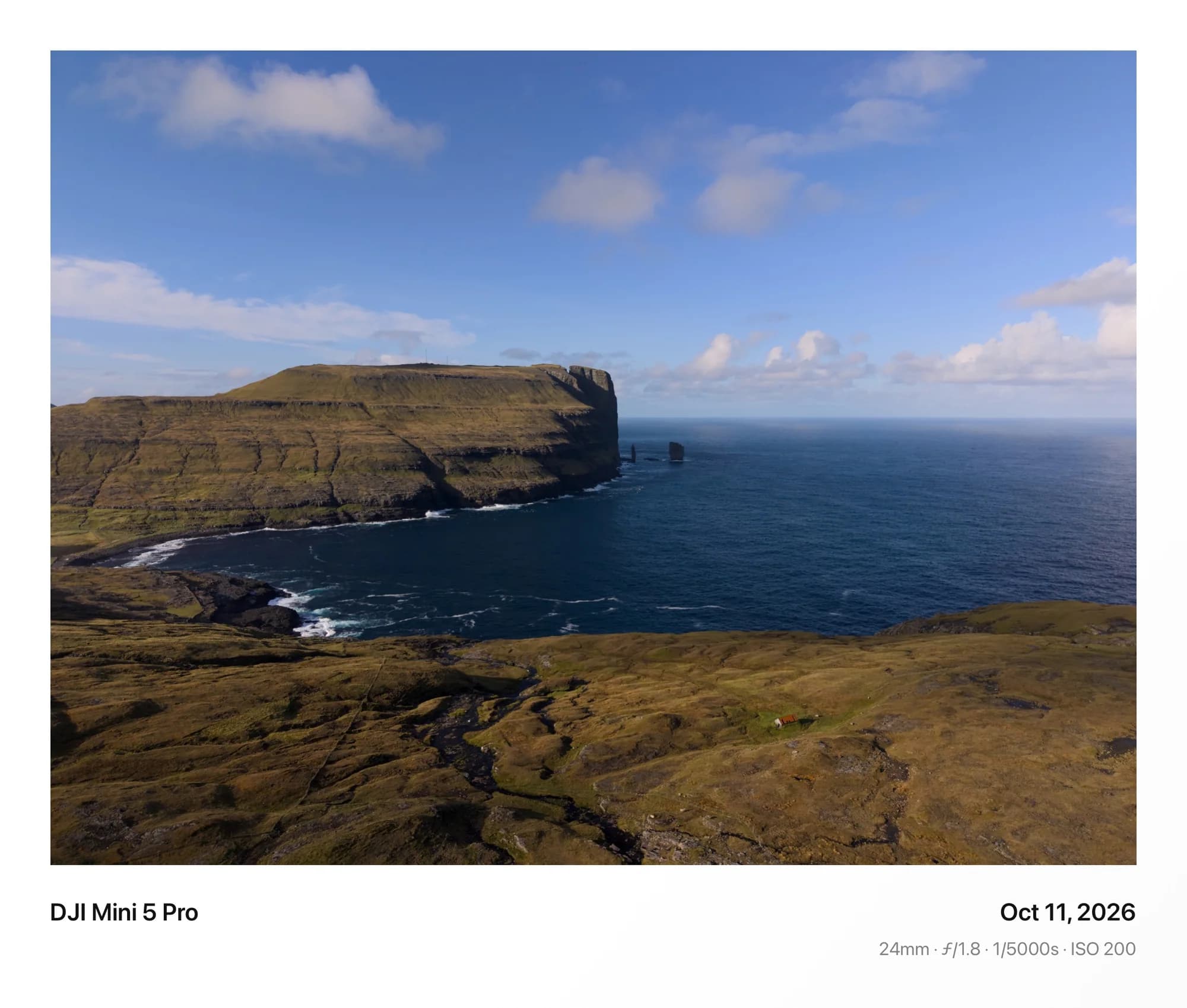 Sea cliffs above a deep blue bay, framed in Classic with the camera details beneath
